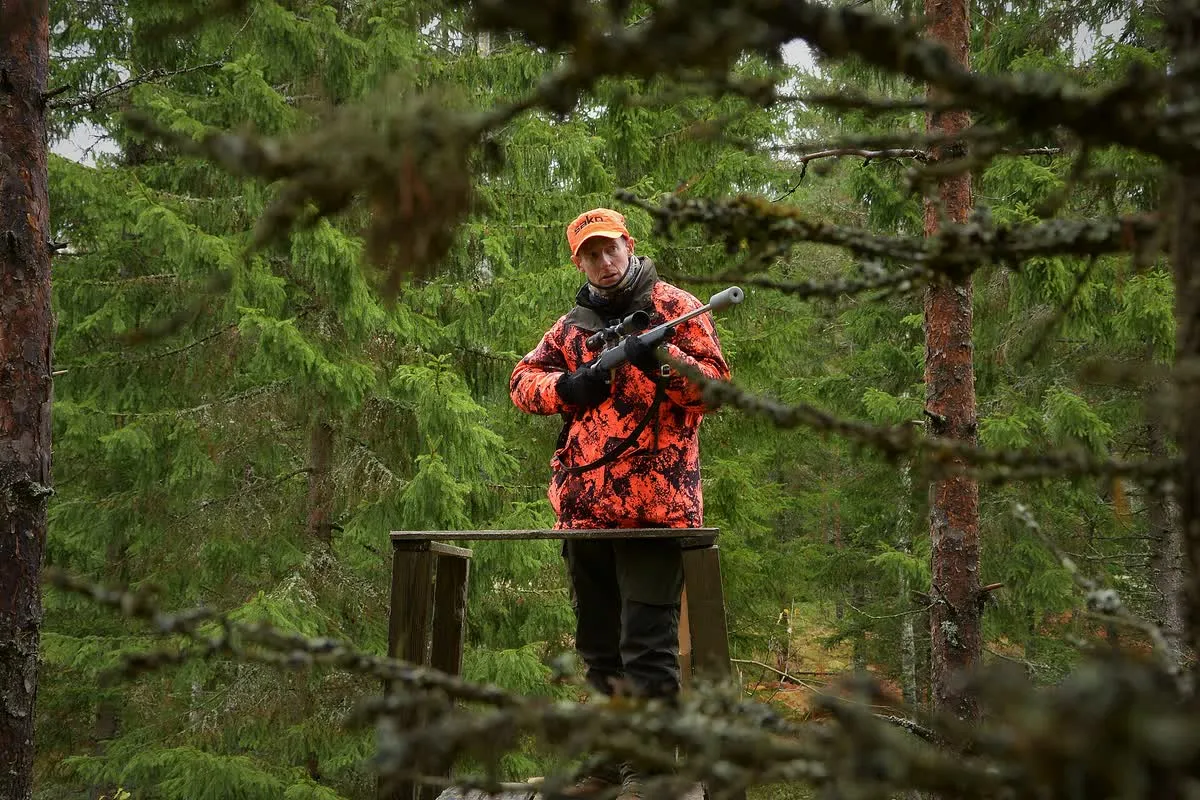 Chasseur en gilet orange fluorescent à l'affût en lisière de forêt